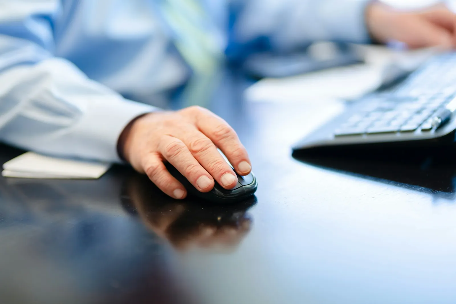 Mano sobre el mouse junto a un teclado, en un escritorio